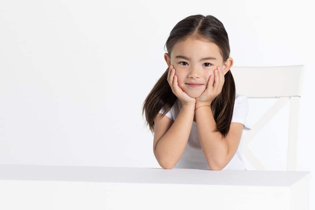 Little Asian girl smiling and holding her face in her hands