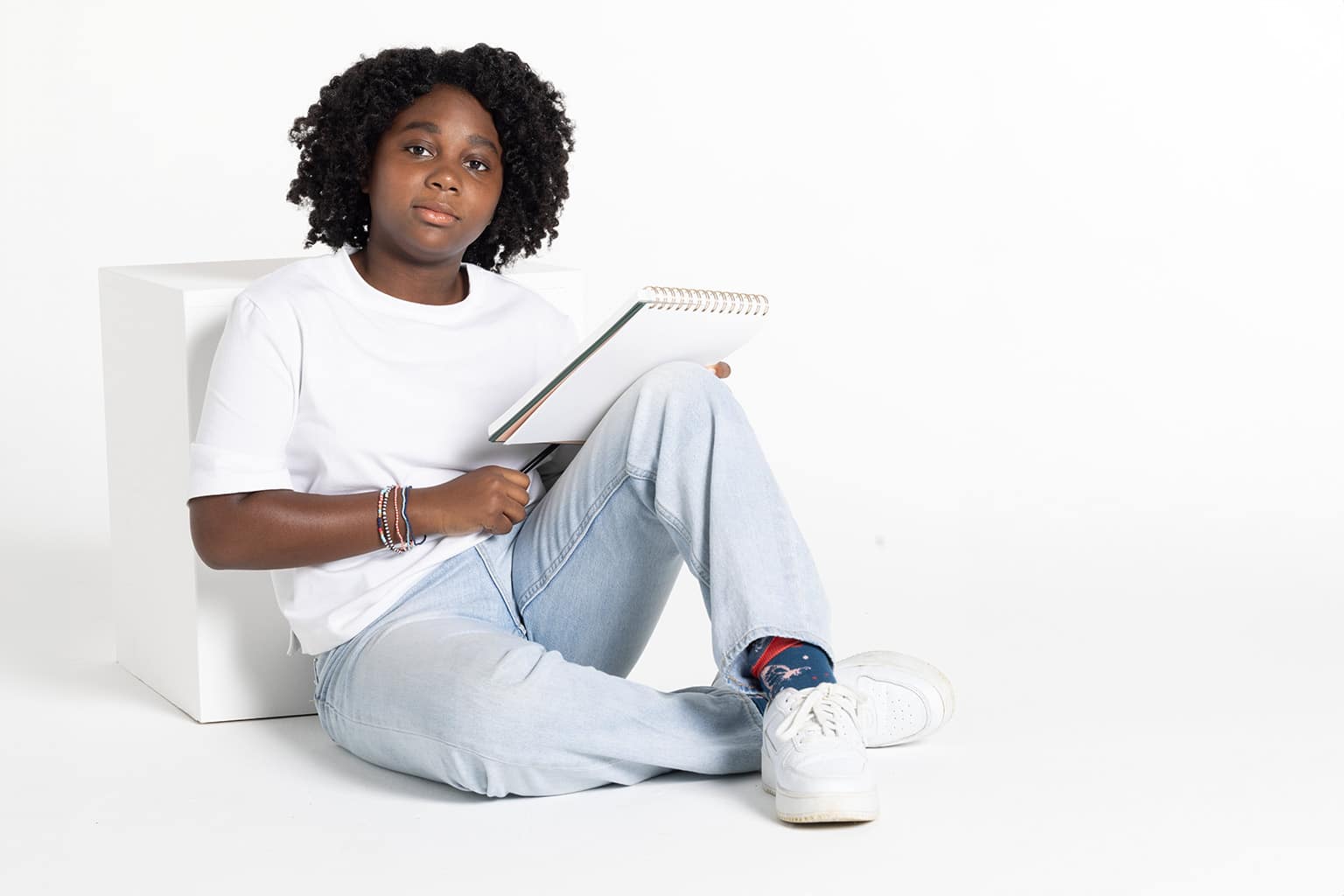 Middle-school aged black girl sitting on the floor with a notebook